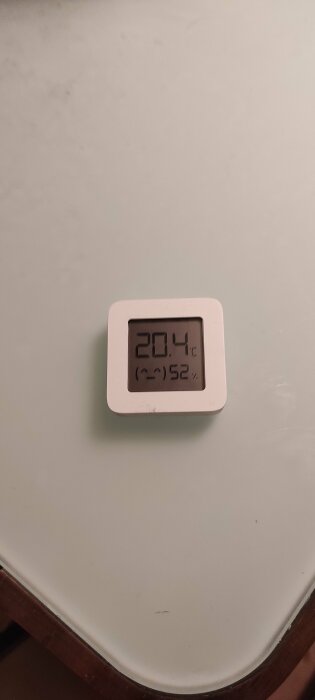 Digital termometer visar temperatur 20.4°C och luftfuktighet 52% på en vit yta.