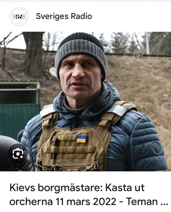 Man i mössa och väst med ukrainska flaggan, utomhus, allvarlig. Sveriges Radio-logotyp, text om Kiev borgmästare.