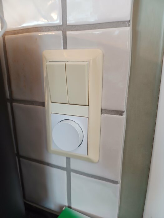 En väggmonterad strömbrytare med en knapp och en vridbar dimmer på kakelvägg.