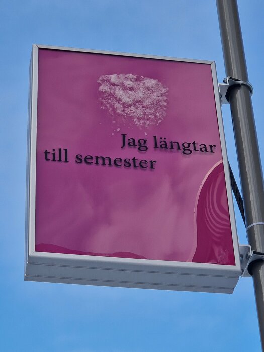 Skylt med texten "Jag längtar till semester" mot blå himmel, rosa bakgrund, vit fläck ovantill.