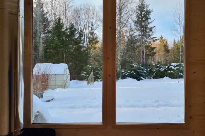 Snöig trädgård sett från ett fönster i trähus, solljus, skogsidyll, fridfullt, vinterlandskap, skjul.