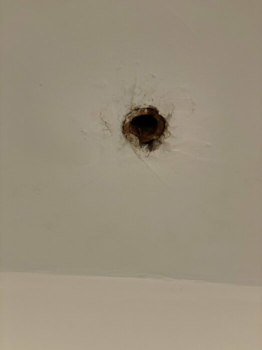 Ett hål i en vit vägg med sprickor och skador runt öppningen.