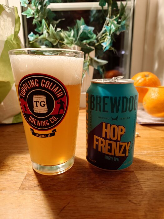 Ett glas ljus öl bredvid en BrewDog "Hop Frenzy" Hazy IPA-burk, apelsiner och gröna växter i bakgrunden.