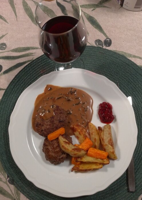 En måltid med köttbullar, gräddsås, lingonsylt, rostade potatisar och morötter. Ett glas rödvin. Hemtrevlig presentation.