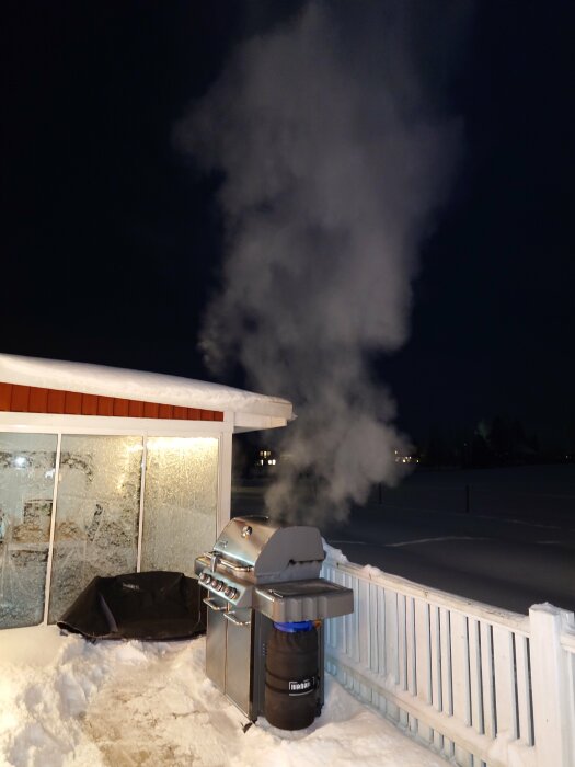 En grill ger ifrån sig rök på en snötäckt terrass om natten.