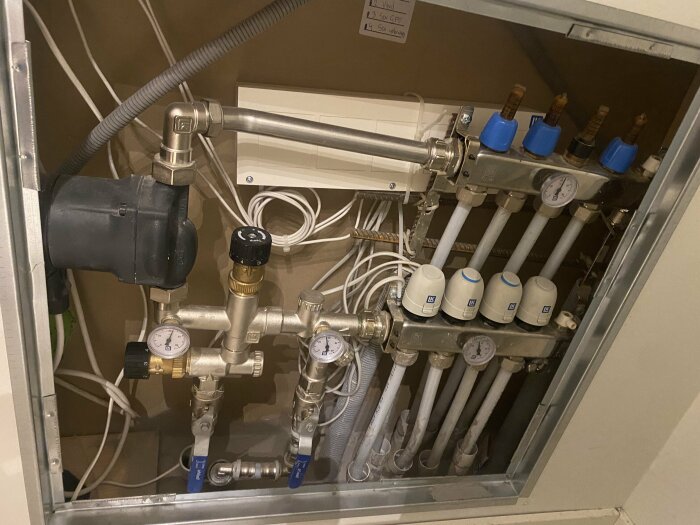 Värmesystem: rör, ventiler, mätare, pump, och manöverdosa i en teknisk alkov.