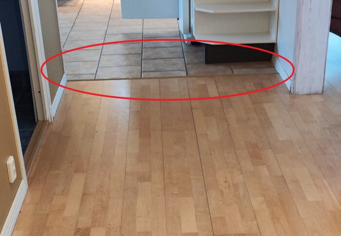Inomhusmiljö med trägolv och plattor, röd cirkel markerar område av intresse, möbel syns, övergång golv till klinker.