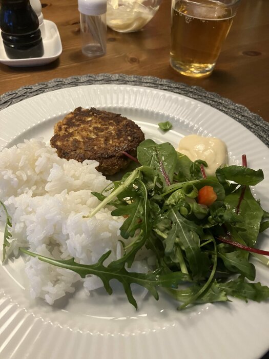 Måltid med ris, vegetarisk biff, blandad sallad, majonnäs på tallrik, peppar- och saltkvarn, vattenglas i bakgrunden.