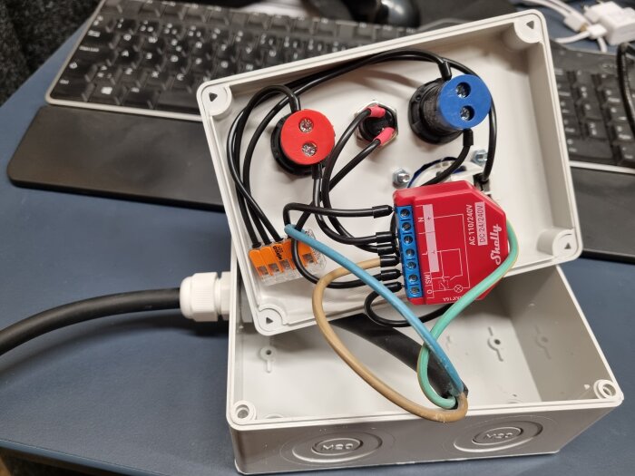 Elprojekt, öppnad kopplingsdosa med elektroniska komponenter, kablar, WAGO-klemmor och relämodul på skrivbord.