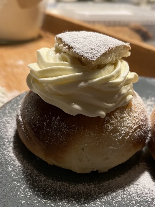 Semla med grädde och mandelmassa, pudrad med florsocker, på en tallrik.