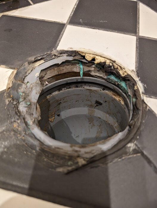 Slitna badrumskakel runt öppet avloppsrör; behov av reparation och rengöring.