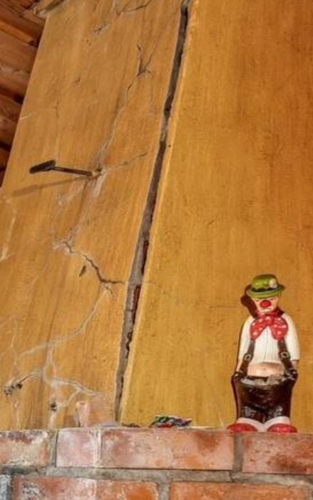En sprucken vägg, mursten nederdel, och en figurin i traditionell klädsel som står vid väggen.