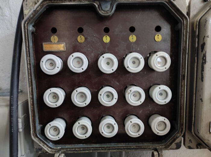 Gammal, möjligen föråldrad elektrisk säkringslåda med keramiska säkringar och numrerade etiketter.