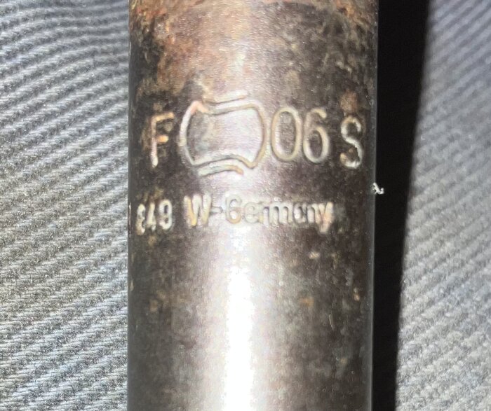 Präglad metall med texten "F 06 S" och "49 W.Germany" på texturerad bakgrund.