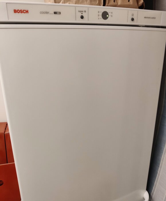 Vit Bosch-kylskåp framifrån, elektronisk kontrollpanel, del av brunt objekt till vänster.