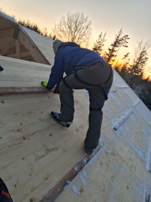 En person arbetar på ett snöbelagt, delvis byggt tak vid skymning.