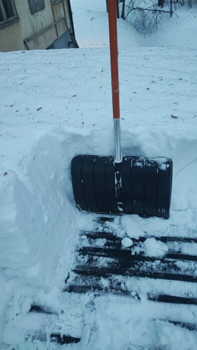 Snöskyffel i snödriva, trätrapp syns, vinterarbete, kallt väder, snöröjning.