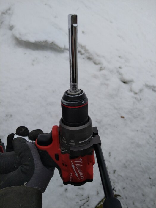 Röd batteridriven borrskruvdragare med bitshållare utomhus mot snöig bakgrund.