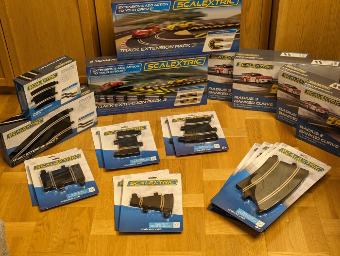 Flera förpackade Scalextric bilbanetillbehör och expansionsset på ett trägolv.