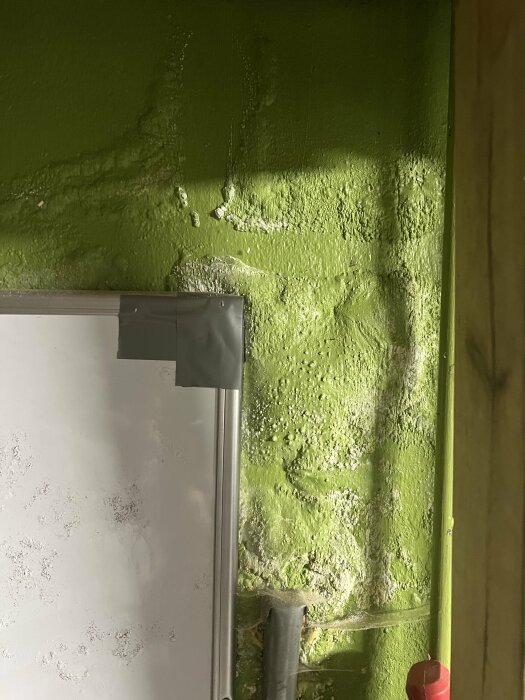 Grön vägg med fuktskador, skadad vitmålning, elledningar, delvis oskarp. Nötning, förfall.