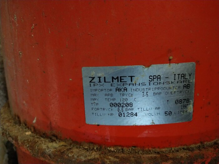 Röd yta med sliten etikett från Zilmet SPA Italy, anger specifikationer för expansionskärl.