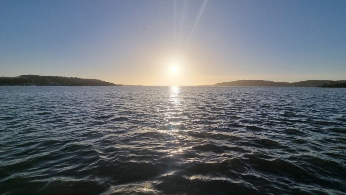 Solnedgång över vattnet, solreflektion, vågigt, klar himmel, horisont, lugnande naturvy.