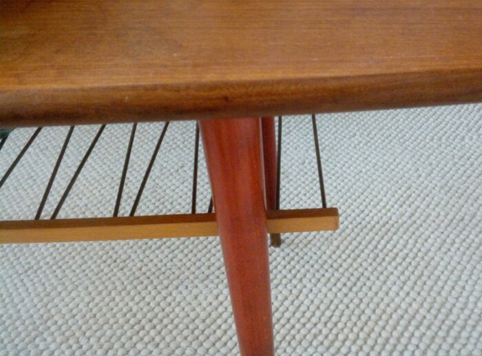 Träbord med rött ben och horisontellt stöd, på strukturerad vit matta.