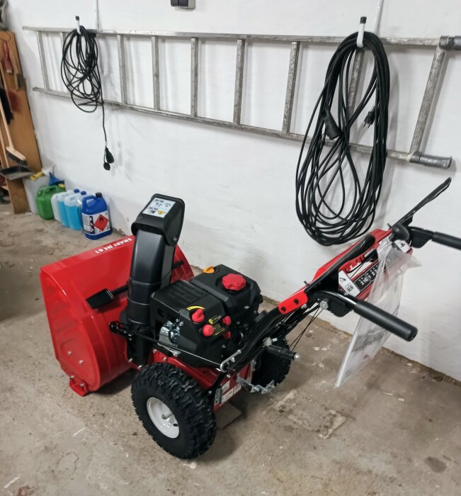 Ny snöslunga i en garage med hängande kablar och bensindunkar.