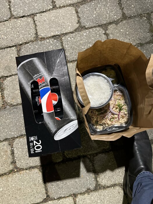 Sneakers och takeout-mat med läsk på en gatstenbelagd yta nattetid.