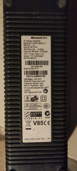 Etikett på Microsoft Xbox 360 AC-adapter med specifikationer och säkerhetsmärkningar. Svart plasthölje. Används för konsol.