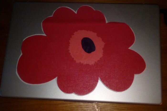 Laptop med röd blomklistermärke på trämöbler i svagt ljus.