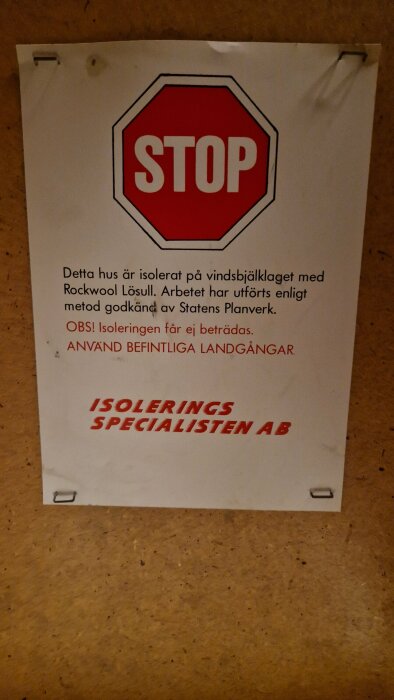 Varningsaffisch om isolering med stoppskylt, instruktioner, och företagsnamn på vägg.