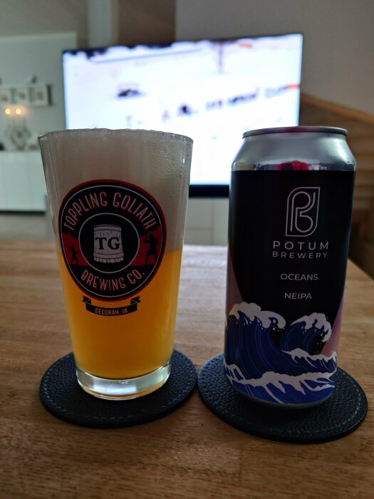 Ett ölglas med öl, en burk, coasters, TV i bakgrunden visar sport.