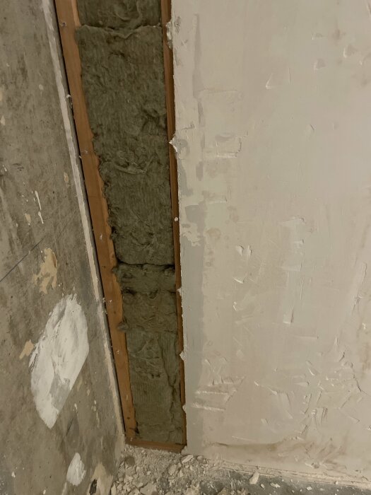 Renovering pågår, öppnad vägg visar isolering, betong och spacklade fläckar. Oavslutat byggarbete synligt.
