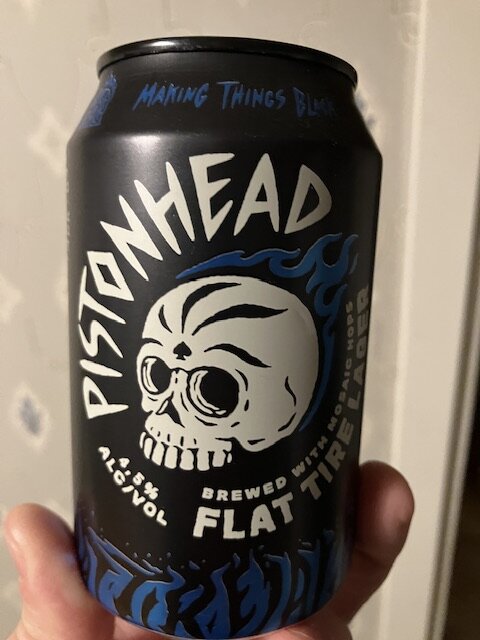 Svart burk med dödskalle, blå lågor, "Pistonhead Flat Tire" logotyp, alkoholhalt märkning.