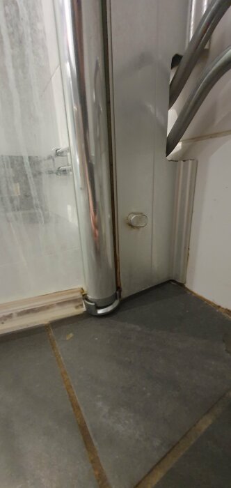 Ett hörn med grått golv och en dörrkarm. Delar av en duschdörr och handtag syns.