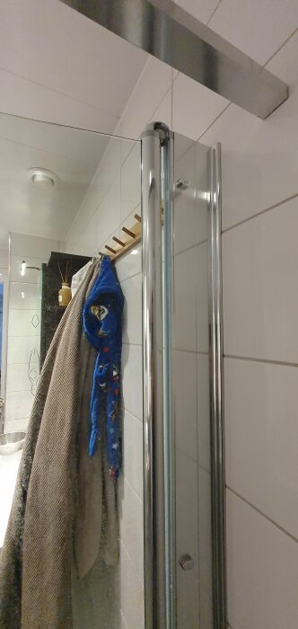 Badrum med duschhörna, handdukar på krok, kakelvägg, och taklampa.