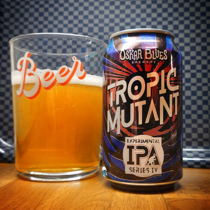 Ölglas märkt "Beer" och ölburk "Tropic Mutant" från Oskar Blues Brewery på rutig bakgrund.