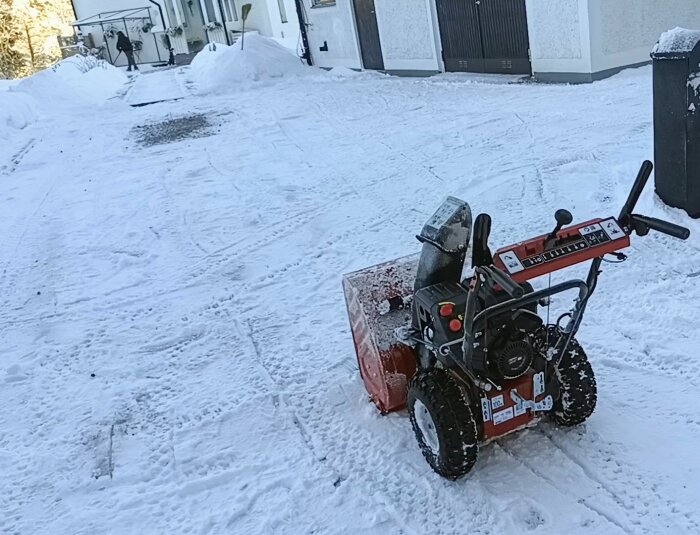 Snöslunga i förgrunden, snöig uppfart, person skottar snö bakgrunden, vintern, dagtid.