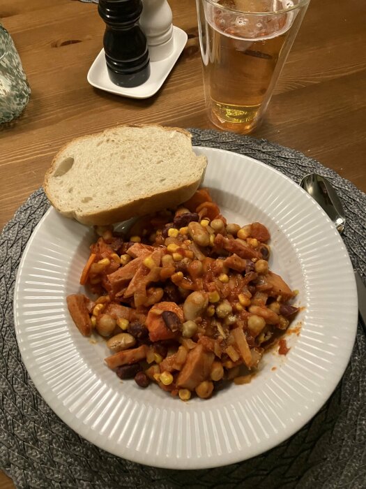 En tallrik med blandade bönor och majs, brödskiva, ölglas, schackpjäser i bakgrunden, på ett träbord.