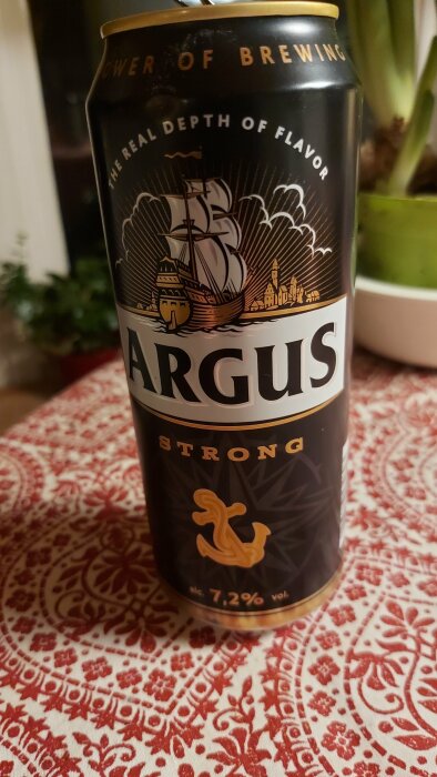 Ölburk märkt "Argus Strong", 7.2% alkohol, segelfartyg, står på mönstrad duk.