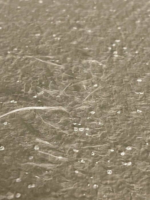 Närbild på en texturerad yta med genomskinliga fibrer och små vattendroppar.