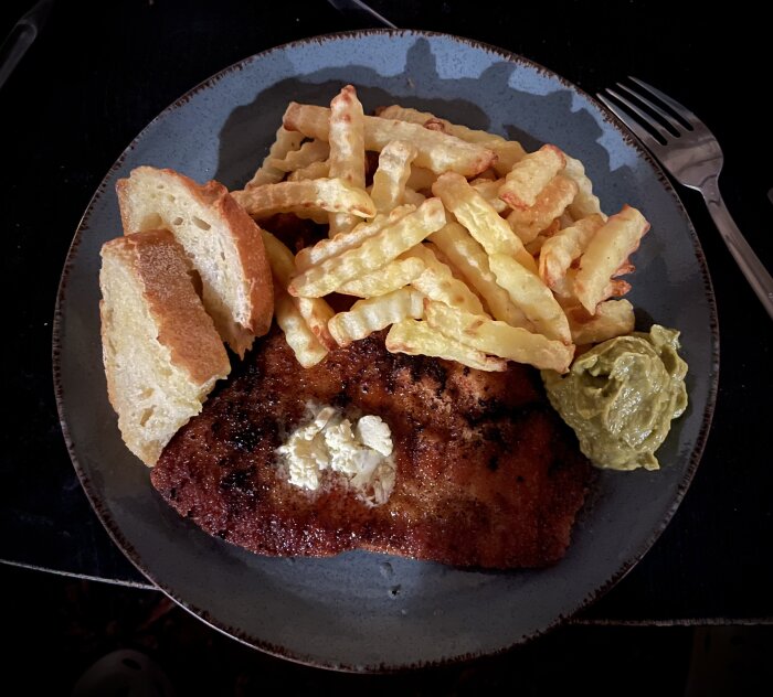 En tallrik med schnitzel, pommes frites, bröd och guacamole. Ljus från vänster skapar kontrast och skuggor.