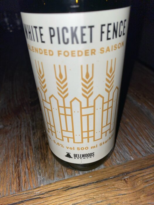 Ölflaska på träyta, etikett säger "WHITE PICKET FENCE Blended Foeder Saison", alkoholvolym 5.6%, 500 ml.