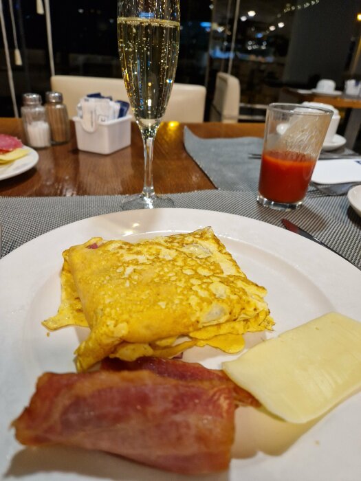 Frukost med omelett, bacon, ost, skumpa och tomatjuice i restaurangmiljö.