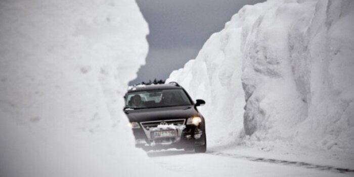 Bil kör mellan höga snöväggar på snöig väg.