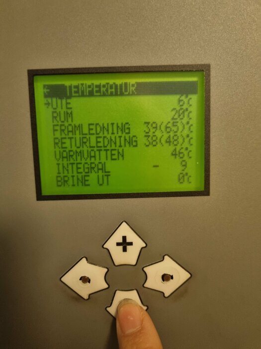LCD-display för värmesystem visar temperaturer, hand justerar inställningar med knappar.