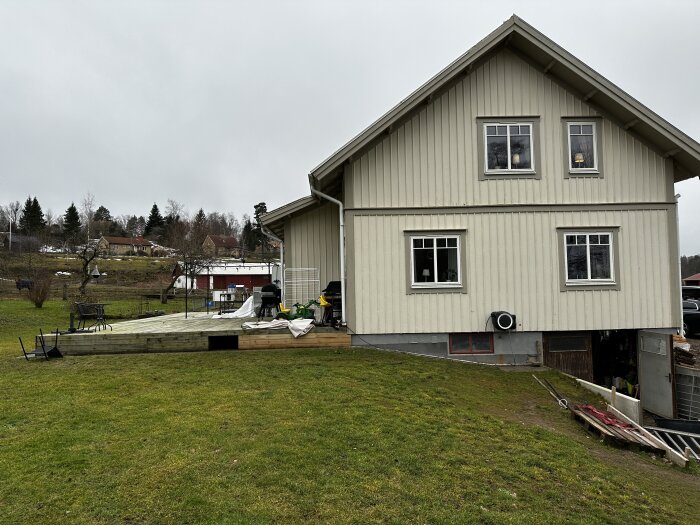 Ett tvåvåningshus med veranda under konstruktion, grå molnig himmel, vått gräs, början av våren.