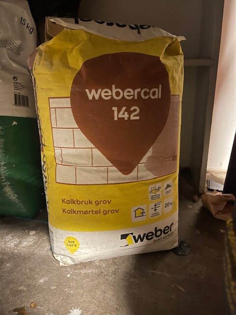 En säck med Webercal 142, grovt kalkbruk, placerad på ett mörkt golv.