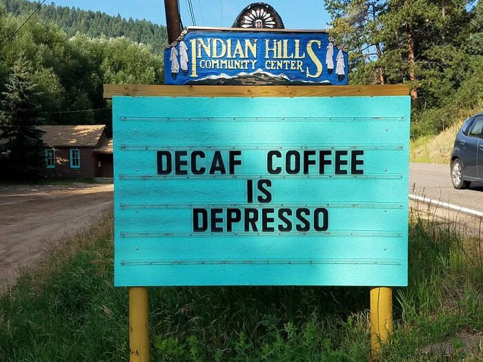 Turkos skylt med ordvits: "Decaf coffee is depresso" framför skog, Indian Hills Community Center.